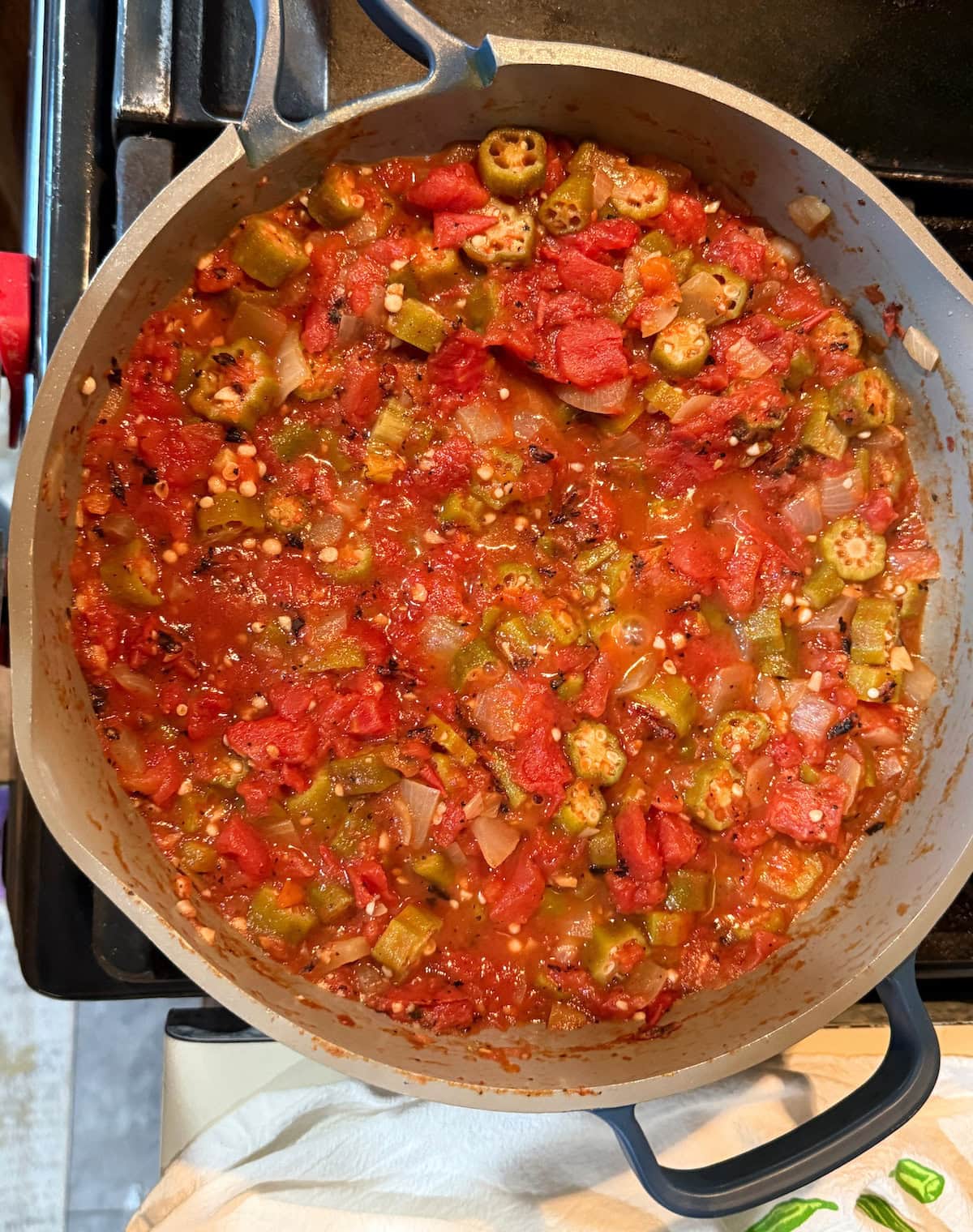 A pot filled with a colorful stew made from diced tomatoes, okra, green peppers, and onions, simmering on a stovetop.
