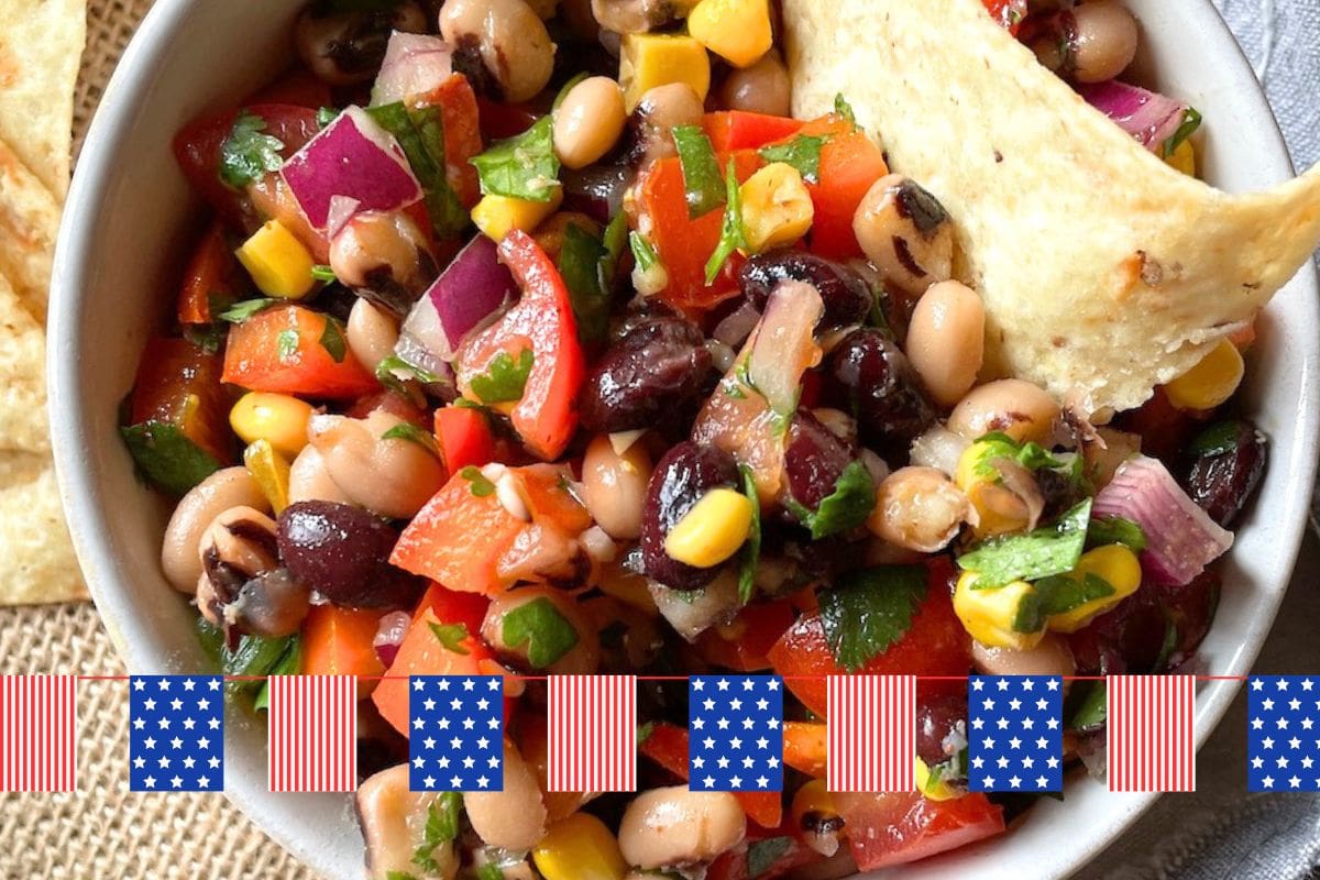 A vibrant bowl of black-eyed pea salad featuring red and yellow peppers, corn, onions, and cilantro, accompanied by crispy tortilla chips.