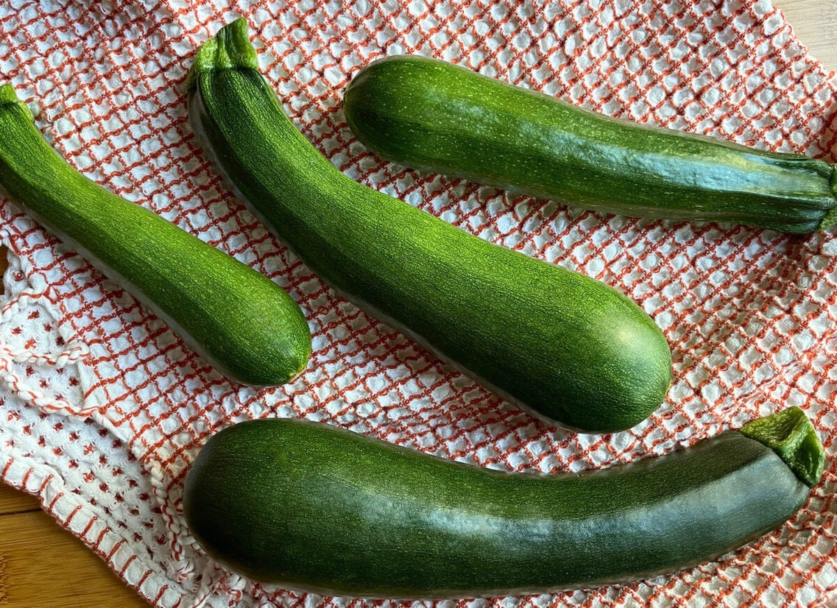 Fresh green zucchinis of various sizes laid out on a textured kitchen towel.