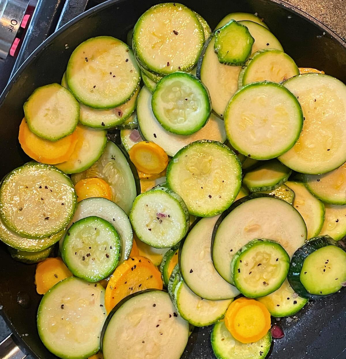 Close-up of sautéed slices of zucchini and yellow squash in a black skillet, seasoned with black pepper.