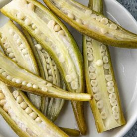 A close-up of freshly cut okra halves displayed on a white plate, showcasing their interior filled with small seeds.