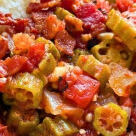 A close-up of a flavorful Southern-style dish featuring sautรฉed okra, tomatoes, and crispy bacon, served alongside a portion of rice.