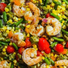 A colorful dish featuring sautรฉed shrimp alongside green beans, corn, okra, and cherry tomatoes, showcasing a mix of vibrant vegetables.