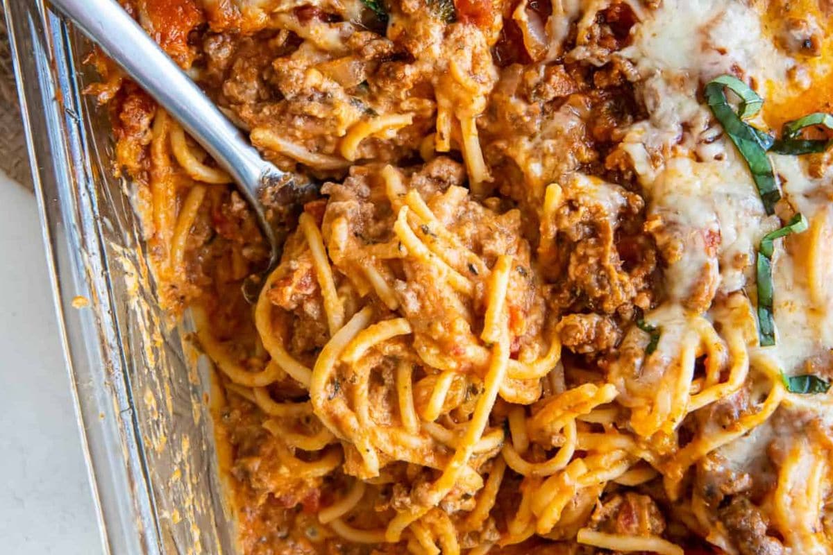 A close-up of a hearty beef spaghetti bake with melted cheese, herbs, and a fork ready to serve.