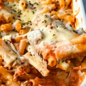 A close-up of a cheesy pasta bake with rigatoni and minced meat, being served with a wooden spatula.
