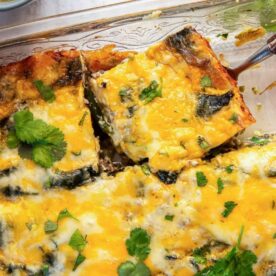 A close-up of a cheesy vegetable casserole topped with fresh cilantro, showcasing a golden crust and layers of ingredients.