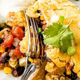 A close-up of a delicious chicken cornbread casserole served with black beans, corn, and fresh cilantro on a white plate.
