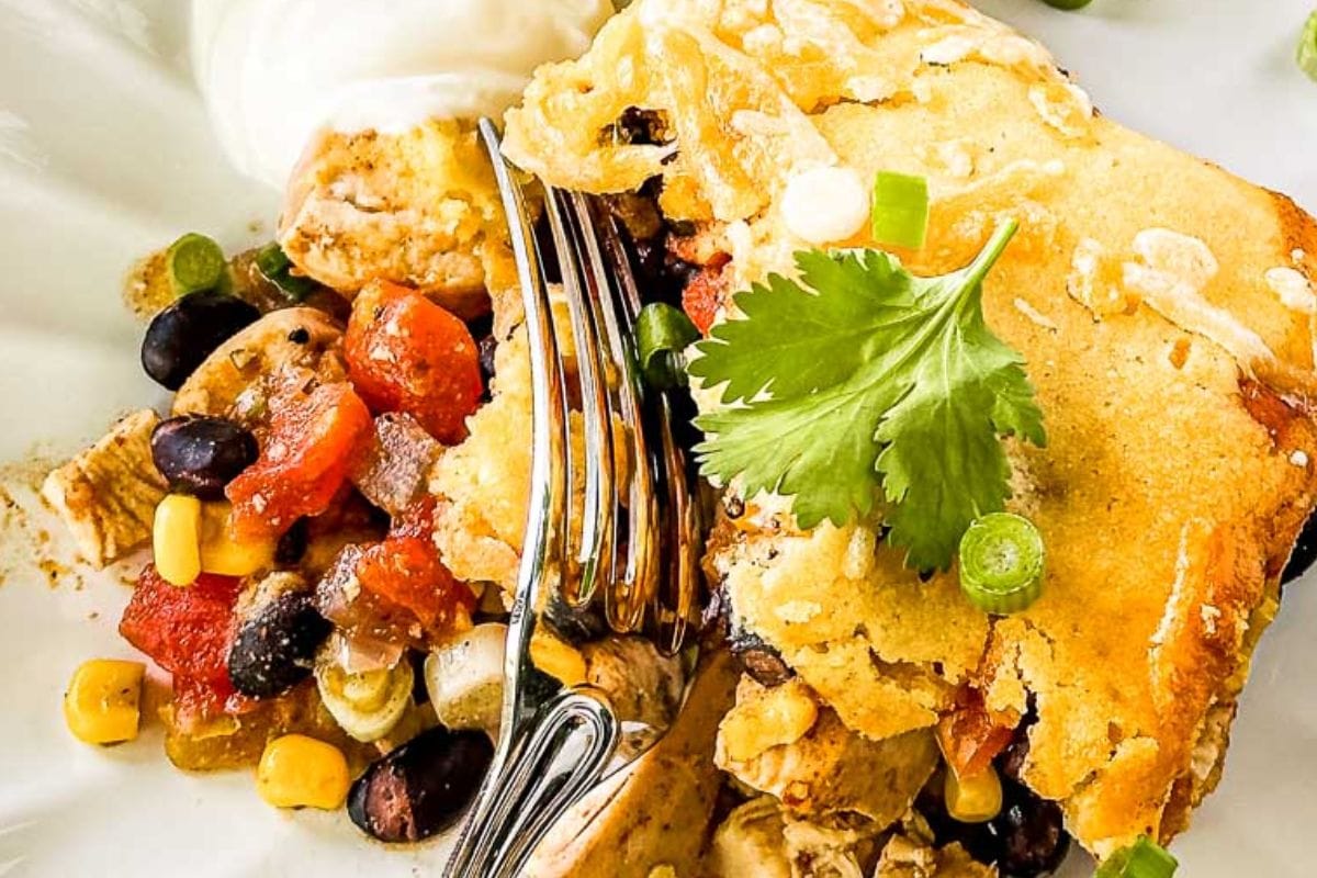A close-up of a delicious chicken cornbread casserole served with black beans, corn, and fresh cilantro on a white plate.