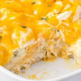A close-up view of a cheesy chicken casserole with melted cheddar cheese and a portion removed, revealing layers of creamy filling and tender chicken.