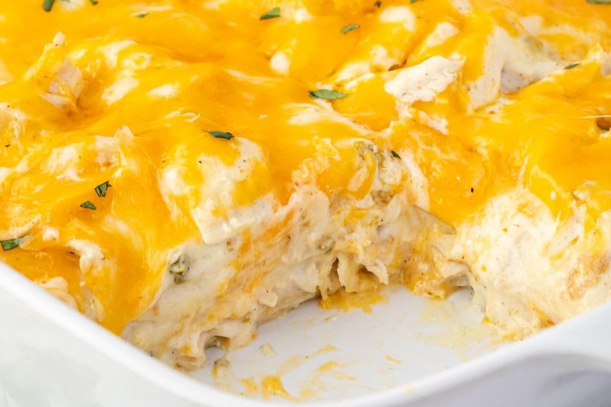 A close-up view of a cheesy chicken casserole with melted cheddar cheese and a portion removed, revealing layers of creamy filling and tender chicken.