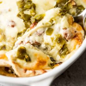 A close-up of a creamy chicken casserole topped with melted cheese and green chiles, showing a serving spoon lifting a portion.