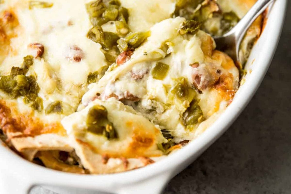 A close-up of a creamy chicken casserole topped with melted cheese and green chiles, showing a serving spoon lifting a portion.