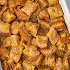A close-up of a golden-brown bread pudding topped with caramelized edges in a white baking dish.