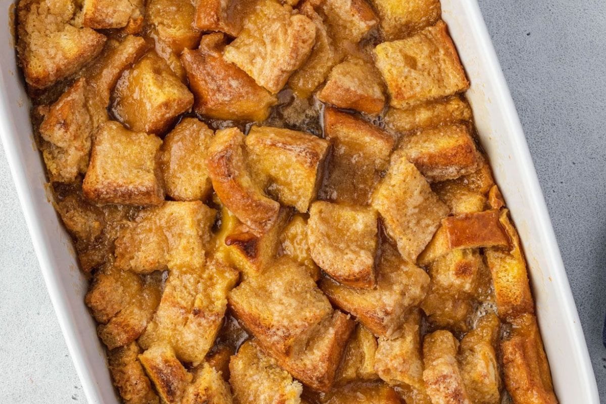 A close-up of a golden-brown bread pudding topped with caramelized edges in a white baking dish.