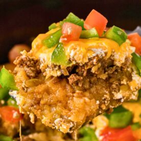 A spoonful of a cheesy beef casserole topped with green peppers and tomatoes, showcasing a hearty mixture of ground beef and rice.
