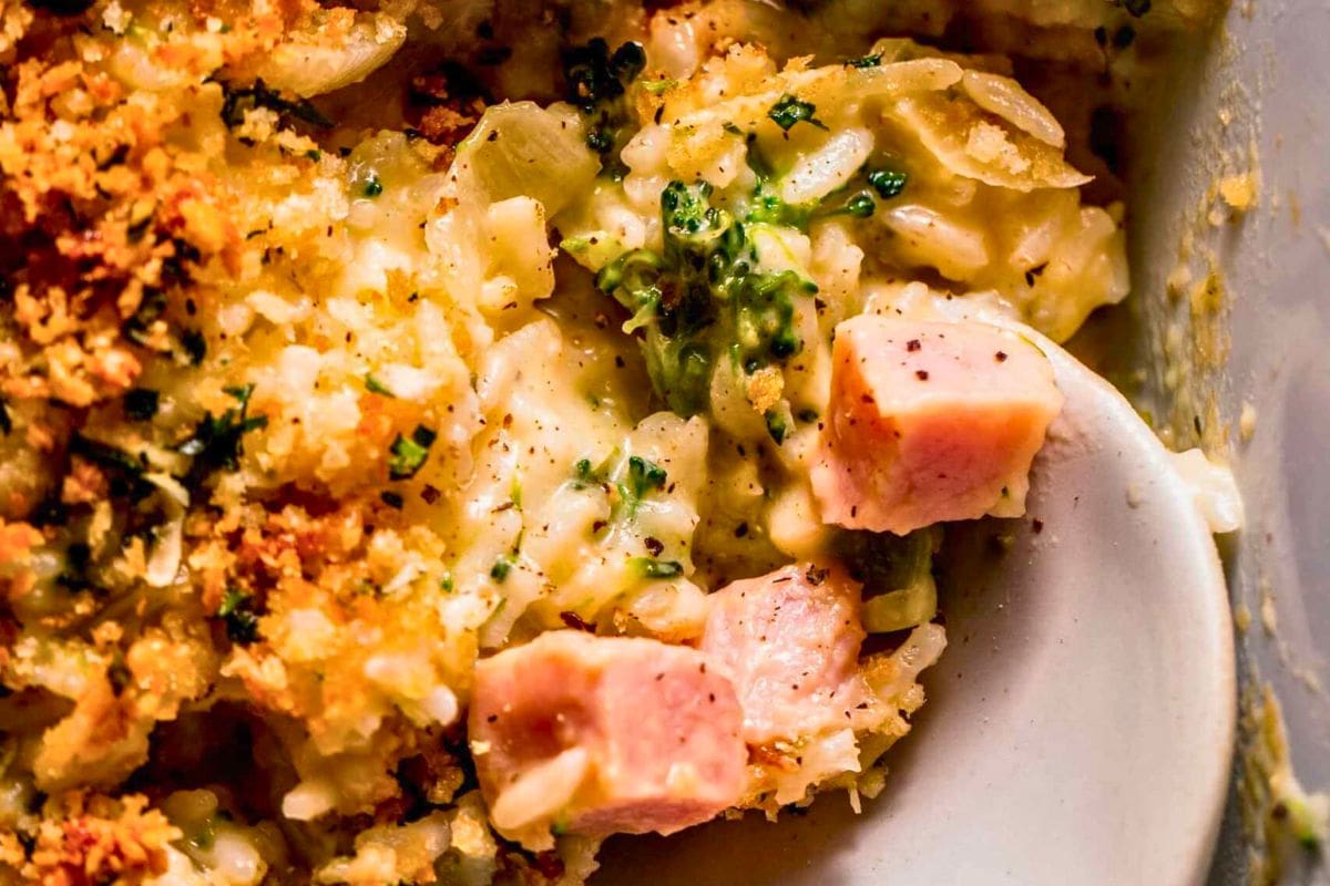 A close-up view of a creamy broccoli and ham casserole topped with a crispy breadcrumb layer, highlighting chunks of meat and vegetables within a rich sauce.