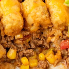 A close-up of a cheesy tater tot casserole with ground beef, corn, and diced tomatoes, showcasing its golden, crispy tater tots on top.