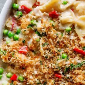 A close-up of a creamy pasta bake featuring colorful vegetables, topped with a golden crispy breadcrumb layer.