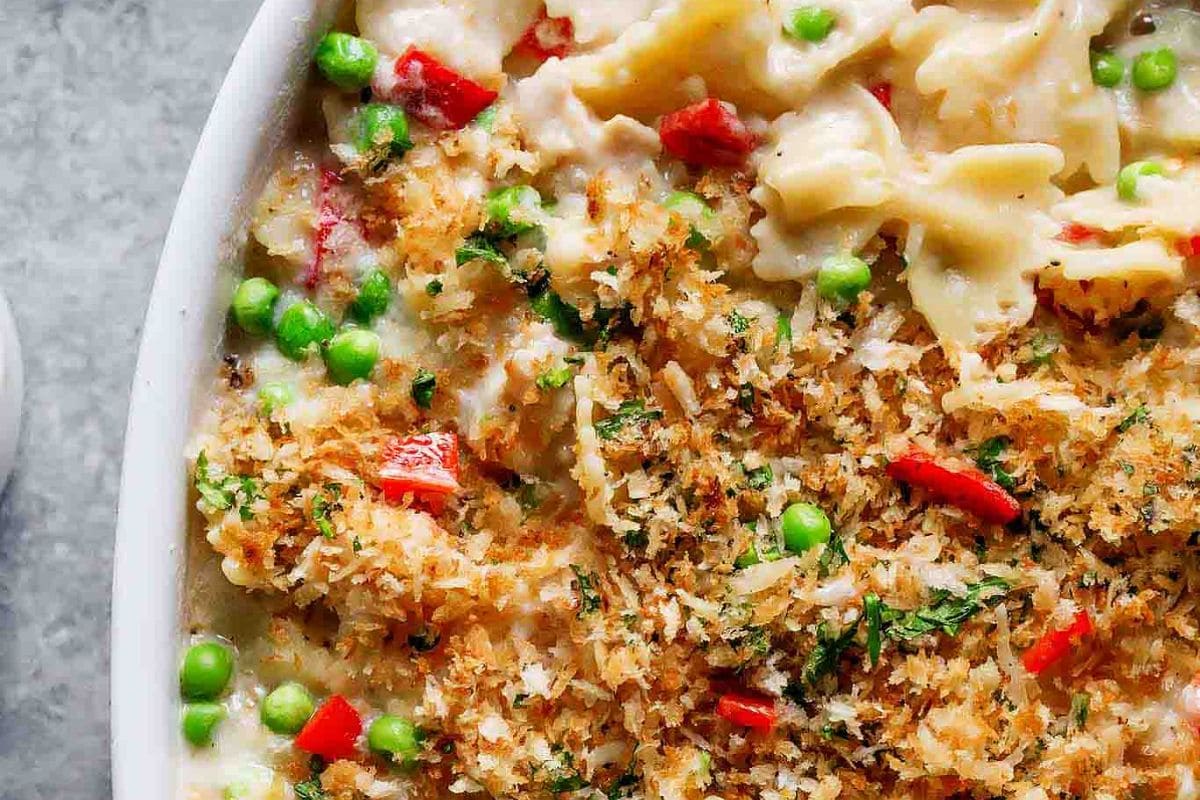 A close-up of a creamy pasta bake featuring colorful vegetables, topped with a golden crispy breadcrumb layer.