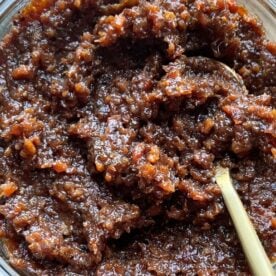 A close-up view of a jar filled with a thick, brown condiment, featuring a wooden spoon embedded in it.