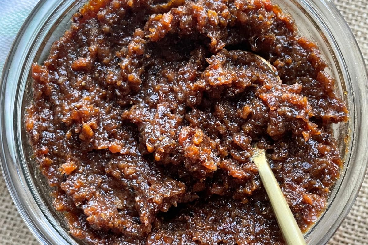 A close-up view of a jar filled with a thick, brown condiment, featuring a wooden spoon embedded in it.