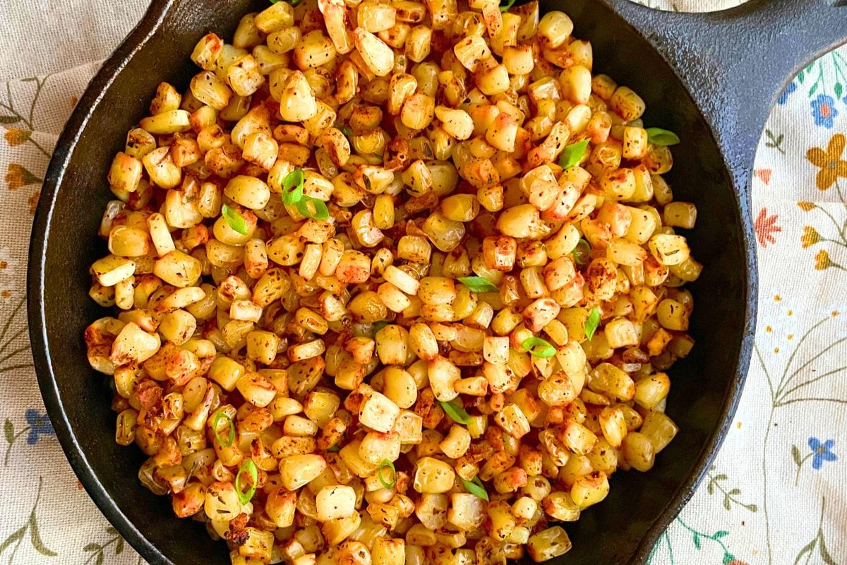 Deliciously roasted corn kernels seasoned and garnished with green onions in a cast iron skillet.