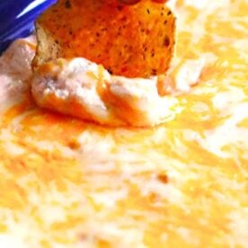 A close-up of a cheesy dip with a tortilla chip being dipped into it, showcasing a rich texture and melted cheese.