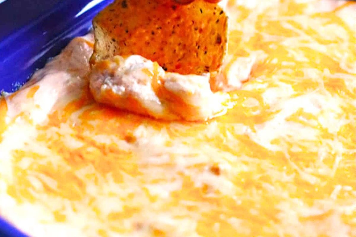 A close-up of a cheesy dip with a tortilla chip being dipped into it, showcasing a rich texture and melted cheese.