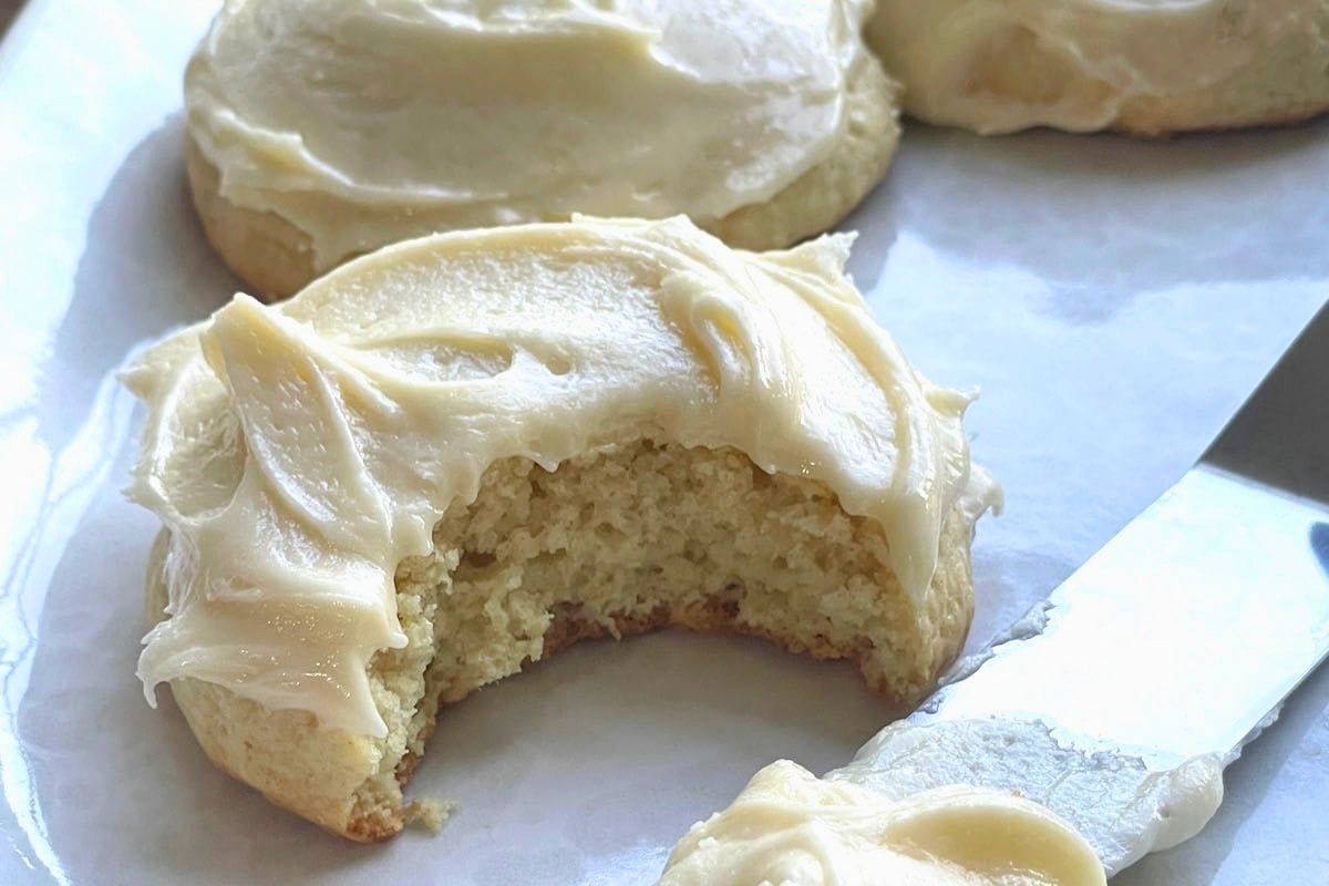 A close-up view of soft sugar cookies topped with creamy frosting, one cookie showing a bite taken out.