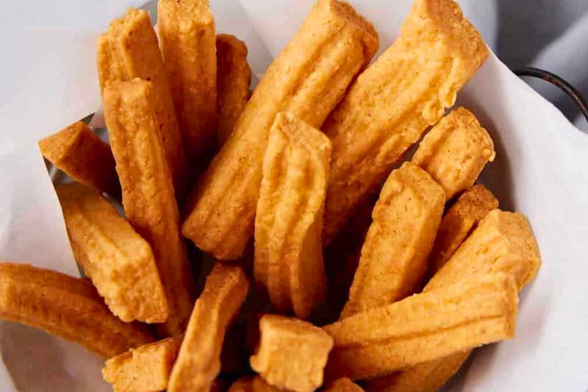 A close-up view of freshly made golden churros, arranged in a basket with a crisp texture.