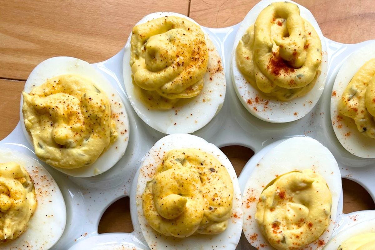 A close-up view of deviled eggs arranged on a white serving tray, garnished with paprika and displaying a creamy filling.