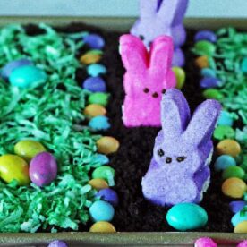 A colorful tray featuring candy bunnies and chocolate eggs on a bed of green grass, creating a festive Easter dessert display.