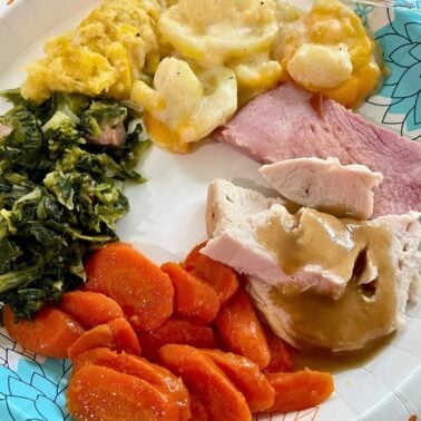 A colorful plate featuring Southern dishes including collard greens, sweet carrots, ham, turkey with gravy, cheesy potatoes, and a cartoon bunny on the side.