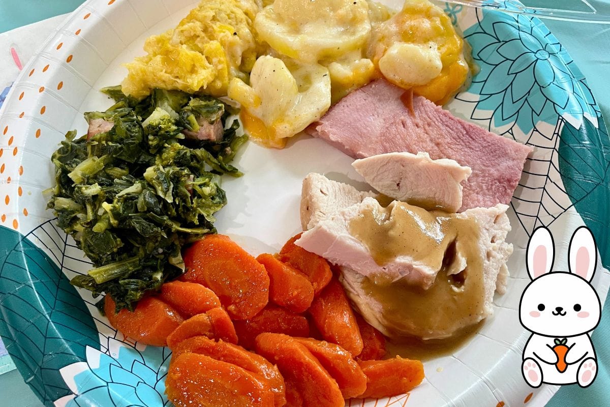 A colorful plate featuring Southern dishes including collard greens, sweet carrots, ham, turkey with gravy, cheesy potatoes, and a cartoon bunny on the side.