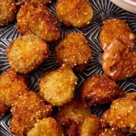 A plate of golden-brown fried pickle slices served with a tangy dipping sauce.