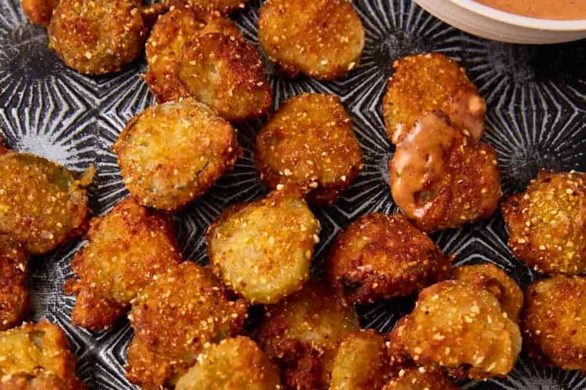 A plate of golden-brown fried pickle slices served with a tangy dipping sauce.