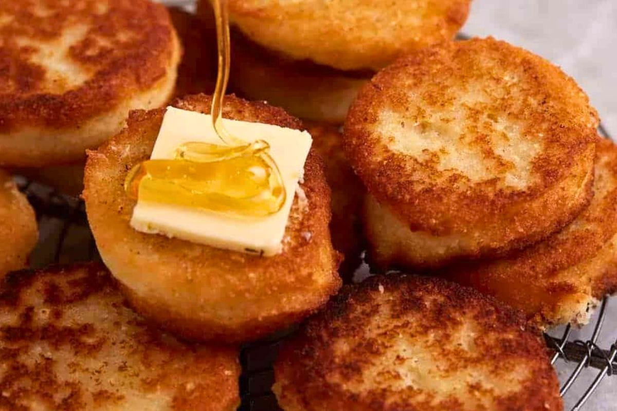 Close-up of crispy golden-brown potato cakes topped with a pat of butter and drizzled honey, resting on a wire rack.
