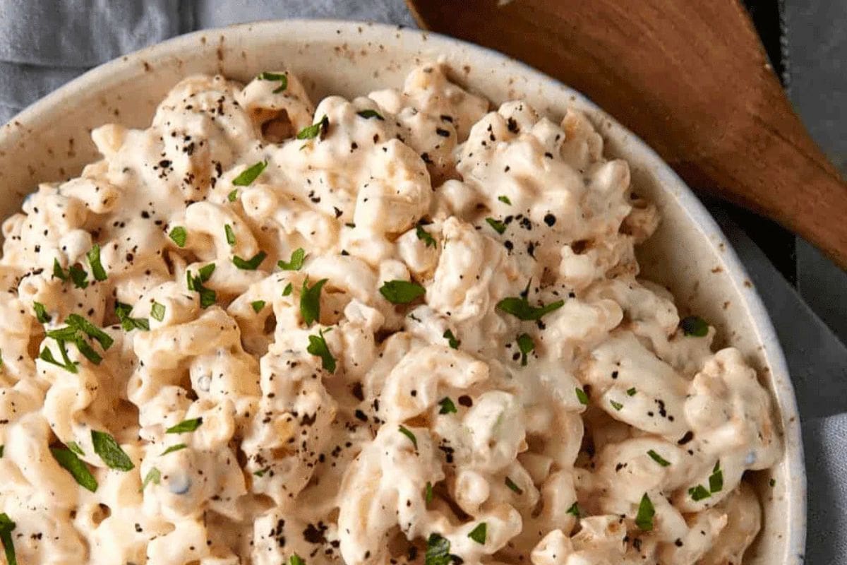 A bowl of creamy pasta salad topped with fresh herbs and black pepper, showcasing a delicious and inviting dish.