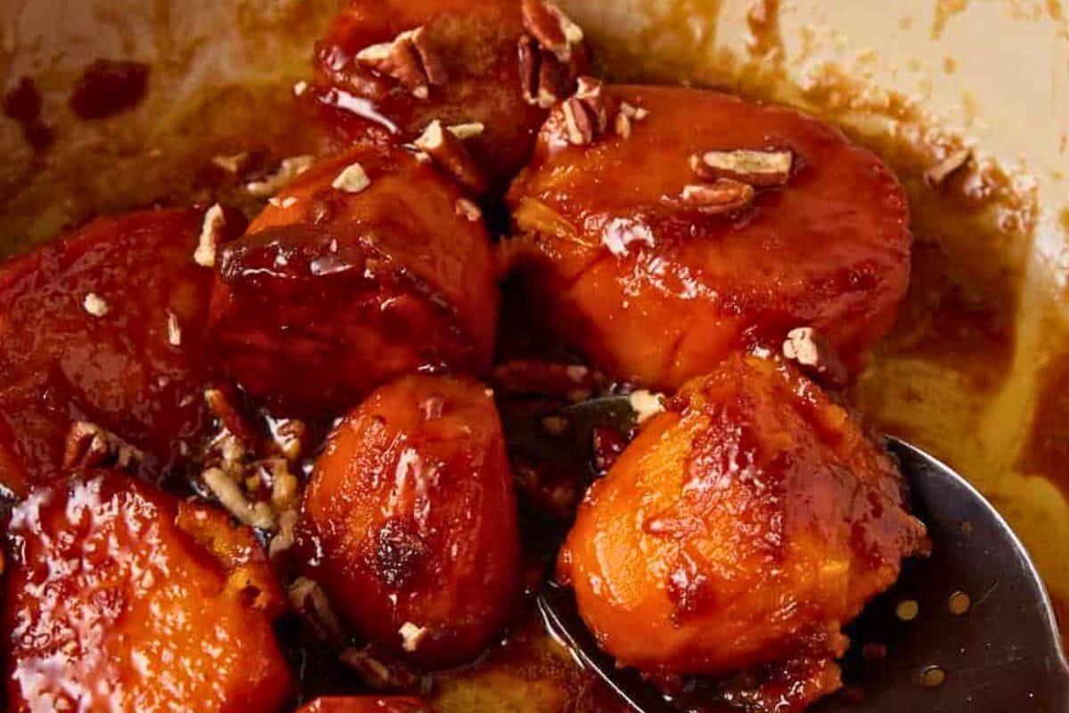 Close-up of caramelized carrots drizzled with syrup and topped with crushed pecans, showcasing a rich, glossy texture.