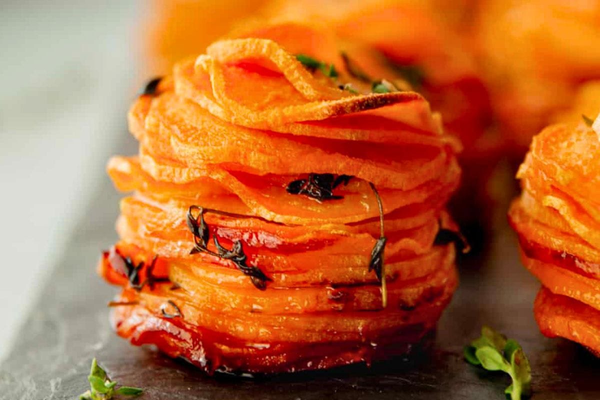 Close-up of layered sweet potato stacks, garnished with herbs, presented on a dark slate surface.